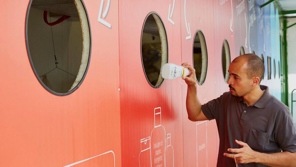 Uomo inserisce una bottiglia di plastica in una grande parete colorata per il riciclo.